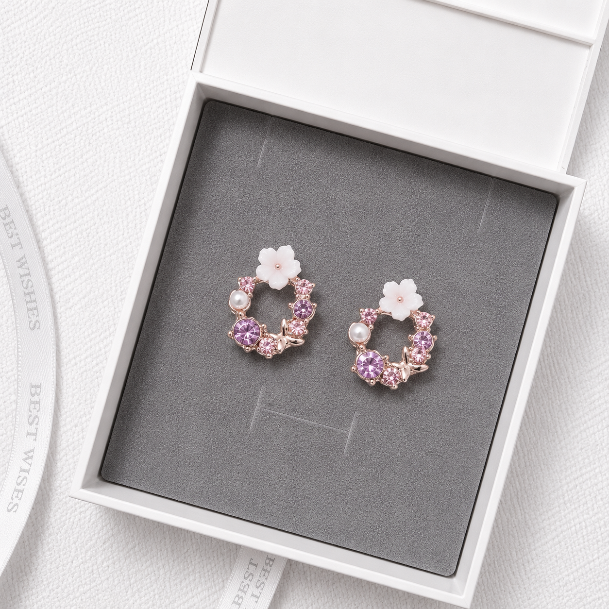 Purple floral crystal stud earrings with pearl accents and rose gold details displayed in a luxury gift box.