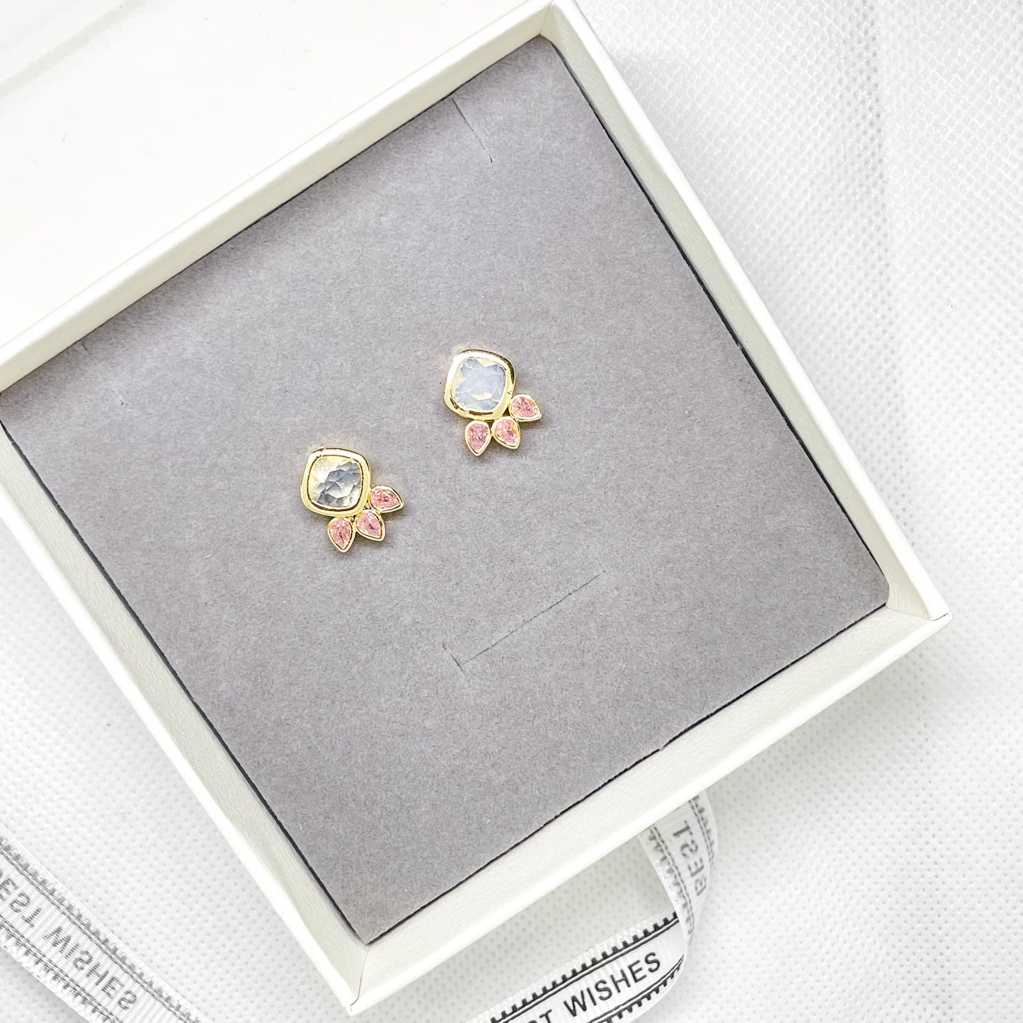 Gold stud earrings with clear crystal and pink crystal details displayed in a jewellery gift box