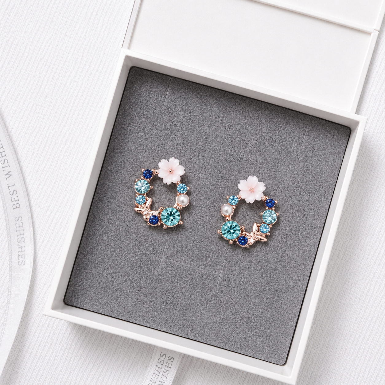 Blue floral crystal stud earrings with pearl accents and rose gold details displayed in a luxury gift box.
