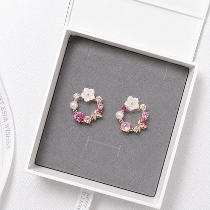 Pink floral crystal stud earrings with pearl accents and rose gold details displayed in a luxury gift box.
