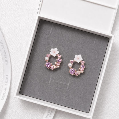 Purple floral crystal stud earrings with pearl accents and rose gold details displayed in a luxury gift box.